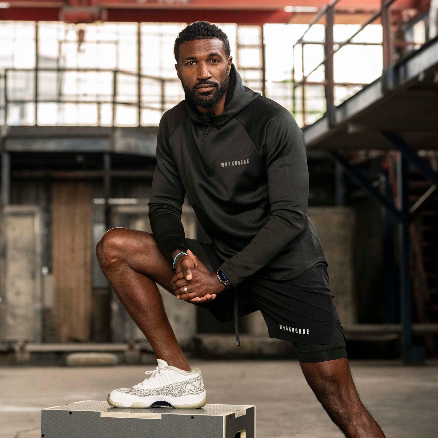 Man wearing Workhorse's High Collar Training Hoodie in black posing in an industrial setting