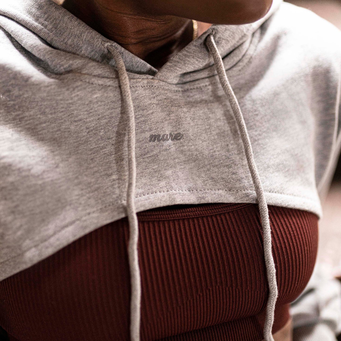 Woman wearing a Mare's Gray Crop Top Hoodie with logo, standing indoors.
