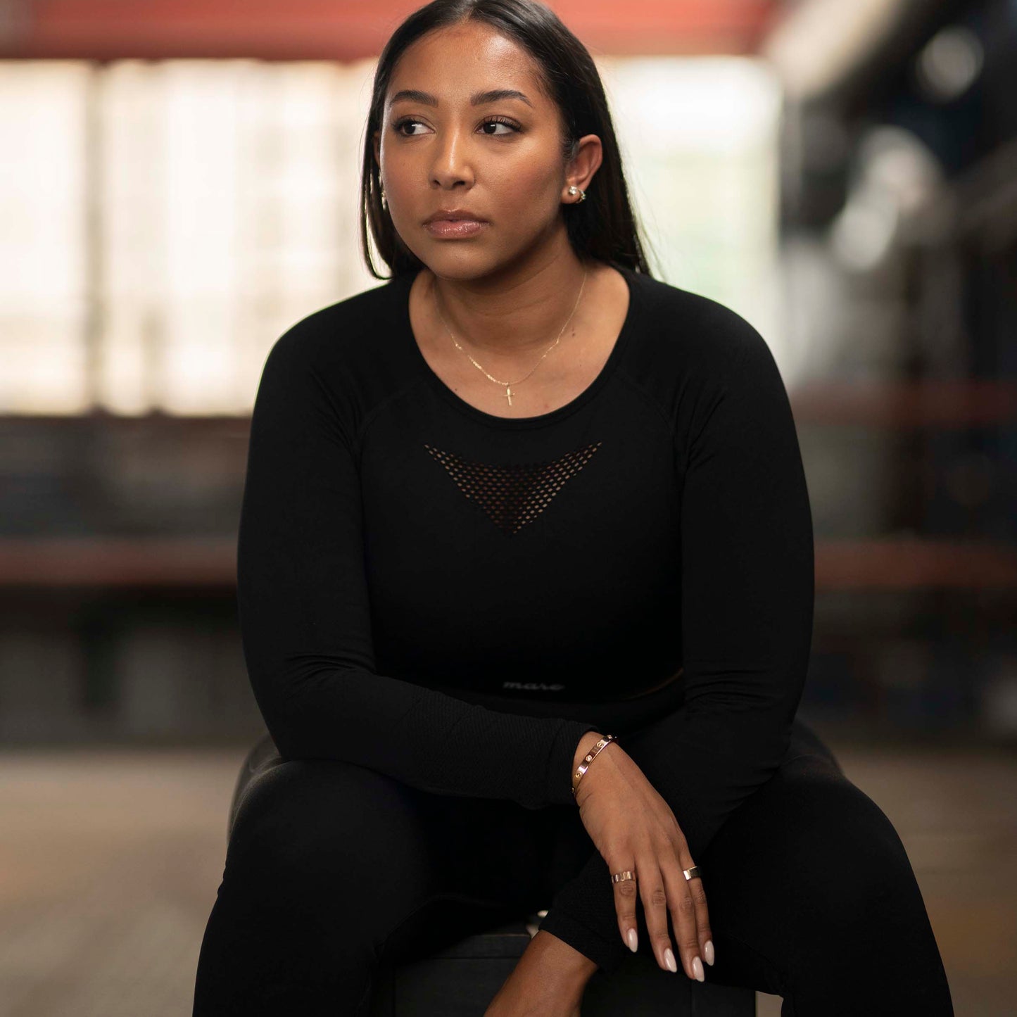 Model wearing Mare's Cropped Long Sleeve Leggings Set in color black sitting in an industrial setting.