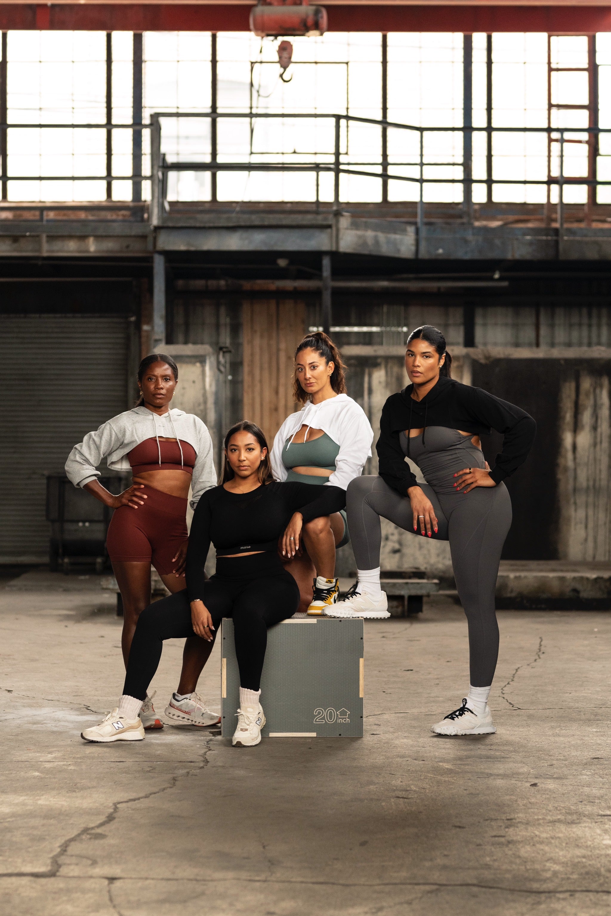 Four women wearing Mare activewear sets and hoodies, posing confidently in an industrial space — women’s performance apparel designed for movement, strength, and style.