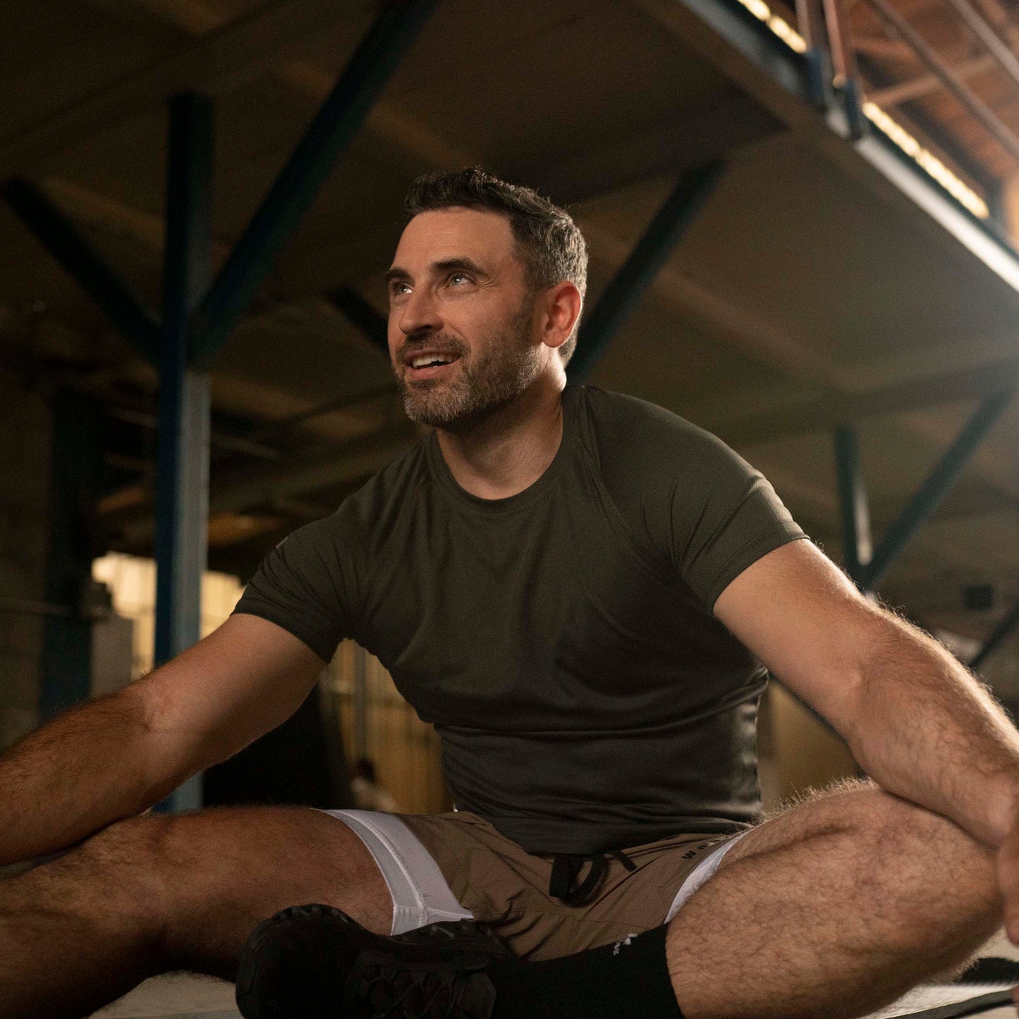 Model wearing Workhorse's Gray Sport Performance T-Shirt sitting on the floor of an industrial setting.