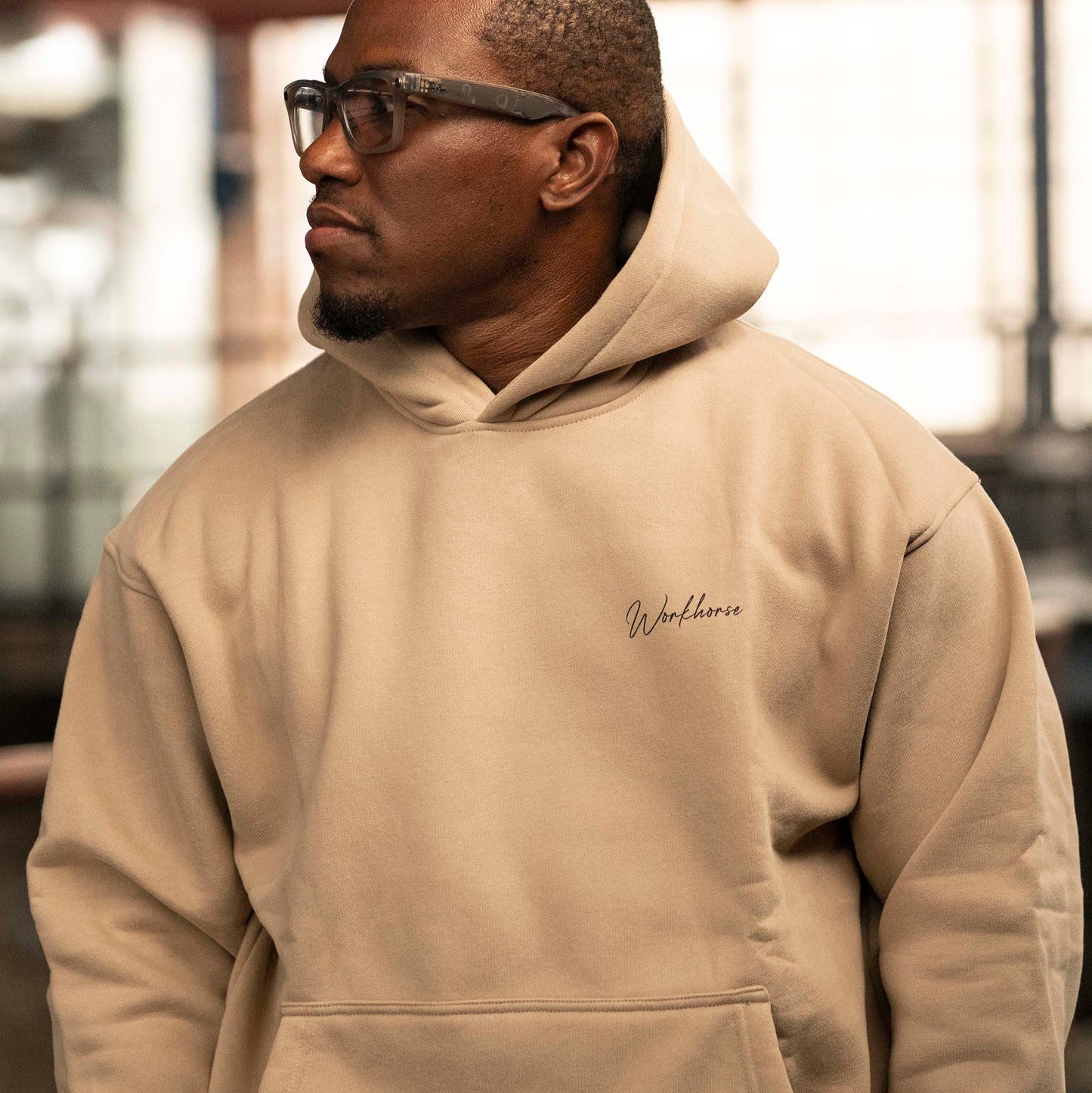 Model wearing Workhorse's Oversize Hoodie in color sand in an industrial setting.