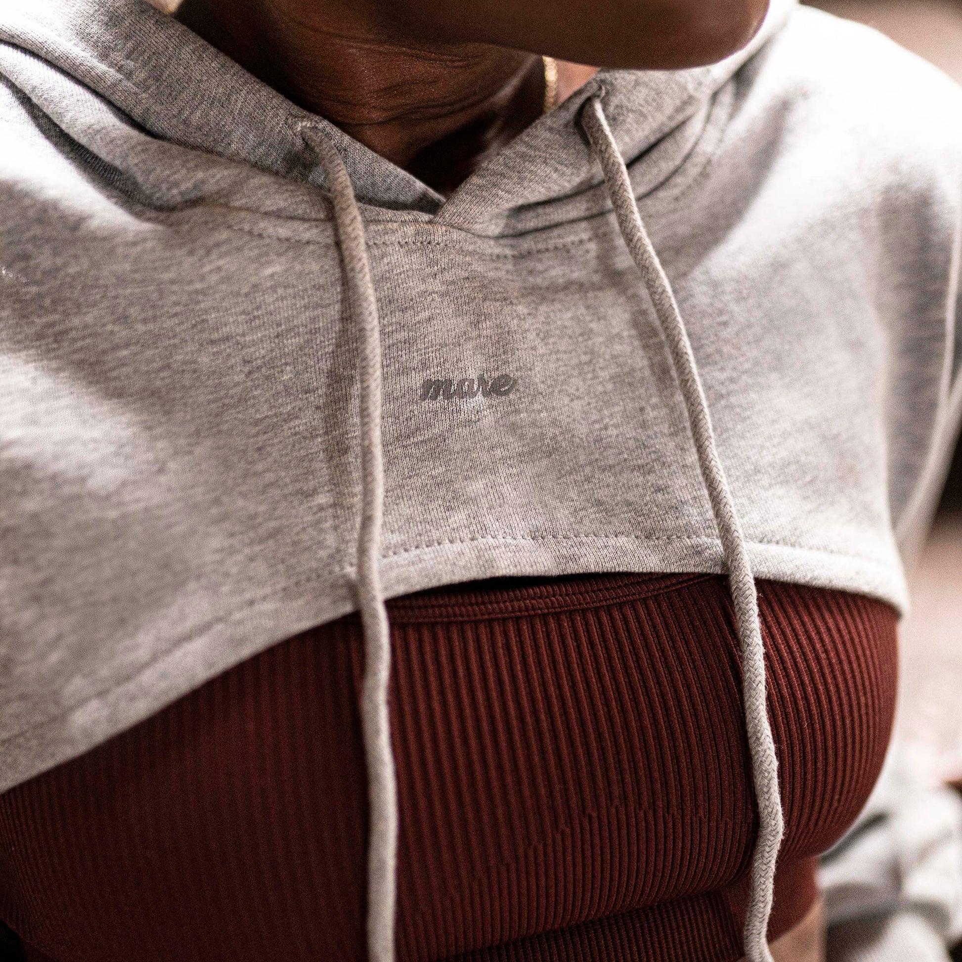 Woman wearing a Mare's Gray Crop Top Hoodie with logo, standing indoors.