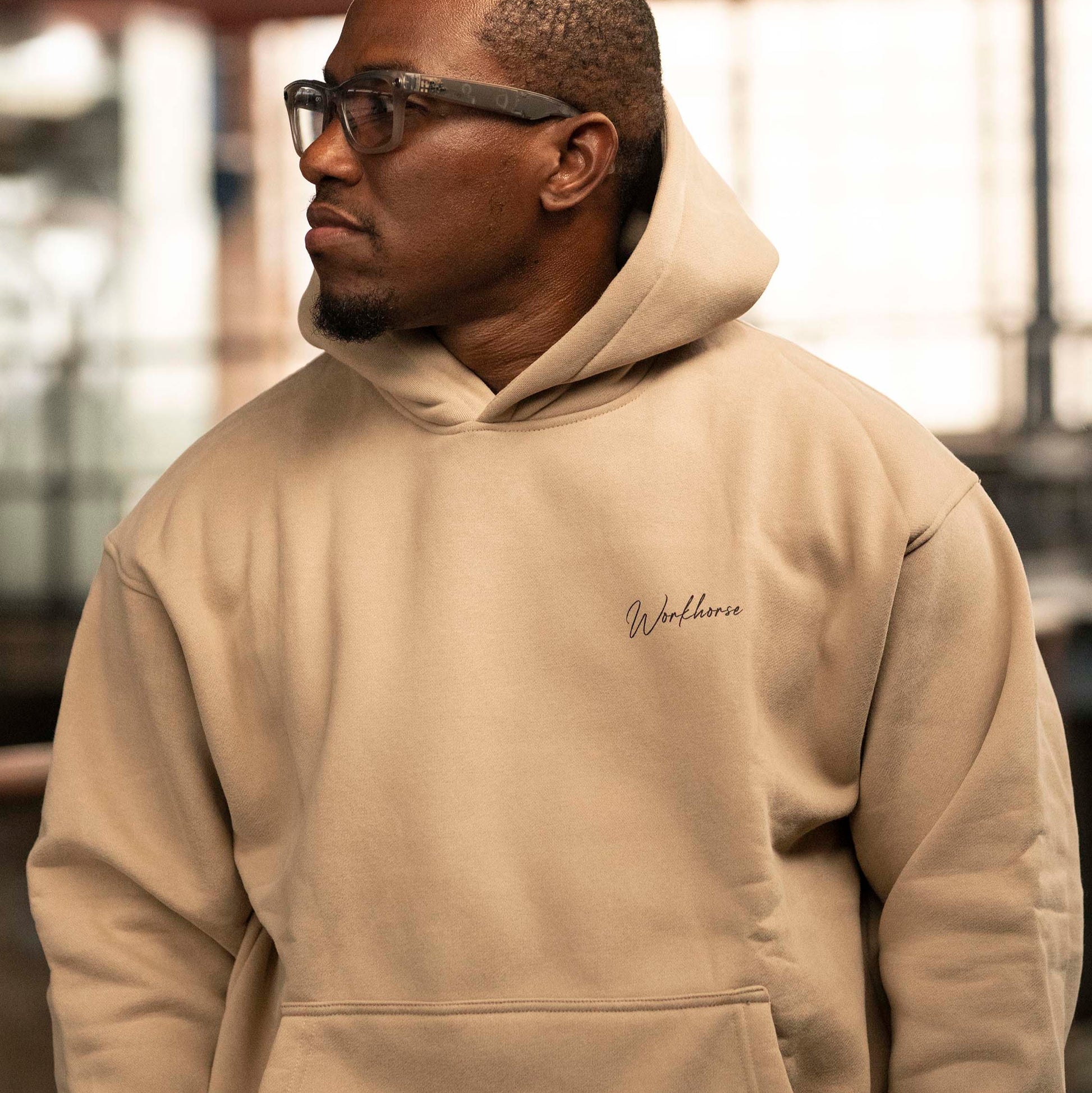 Model wearing Workhorse's Oversize Hoodie in color sand in an industrial setting.